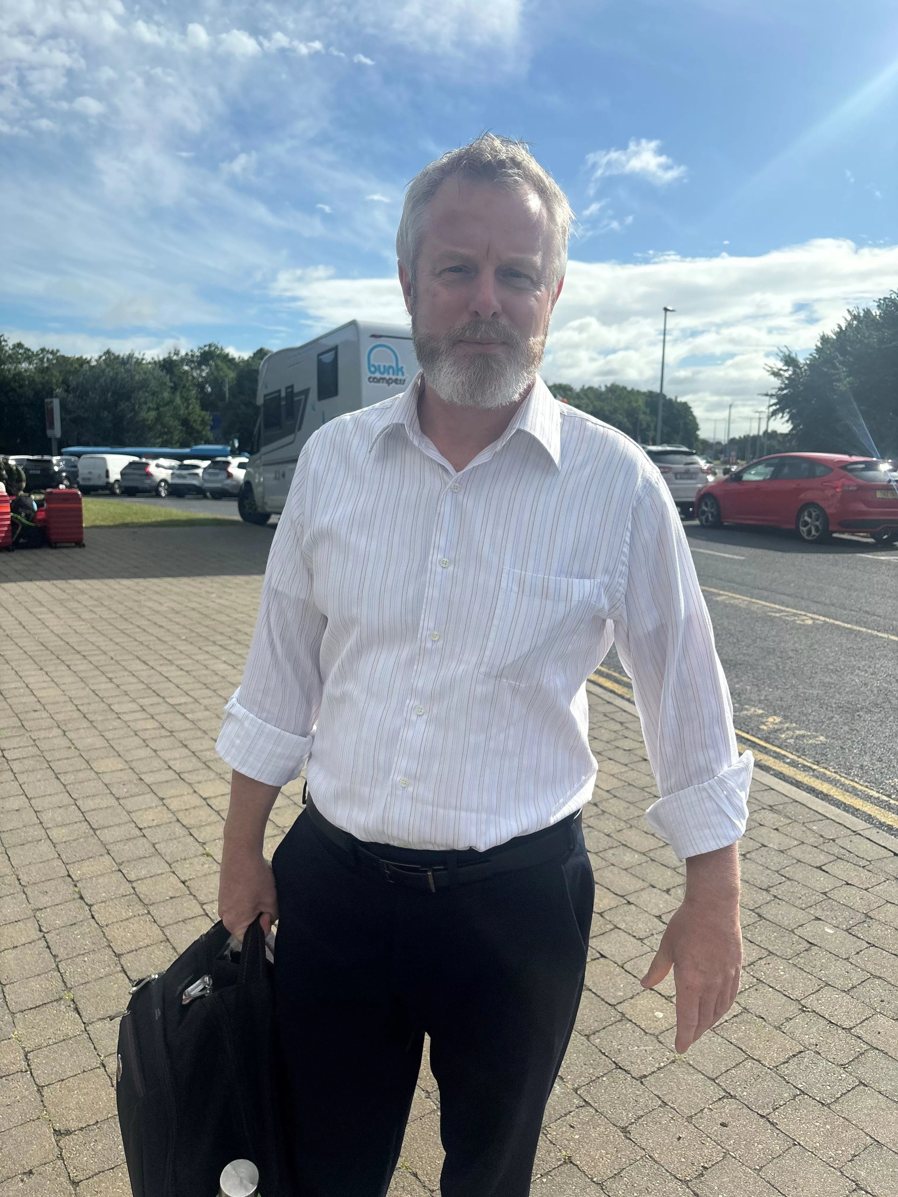 Mark Tighe pictured in shirt and suit trousers, carrying a bag