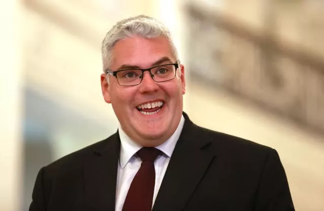 Head and shoulders photo of DUP leader Gavin Robinson in a black suit, smiling