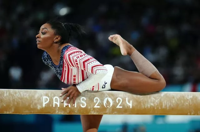 Simone Biles, with one leg off the bar and another resting on it. 