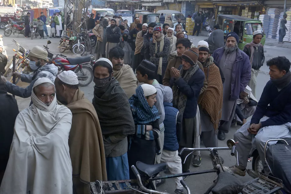 People stand in a long queue and wait to buy subsidised sacks of wheat-flour from a sale point in Peshawar, Pakistan