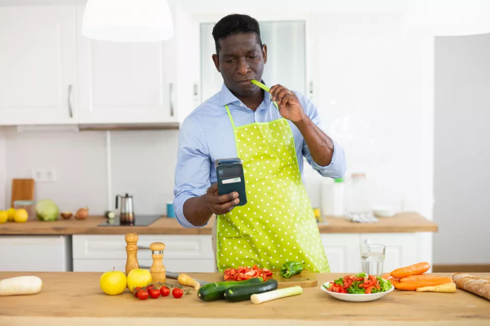 A black middle aged man in the kitchen cooking and chopping veg, wearing a lime green apron