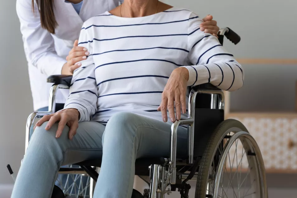 Close up of woman in white coat helping woman in wheelchair in medical setting