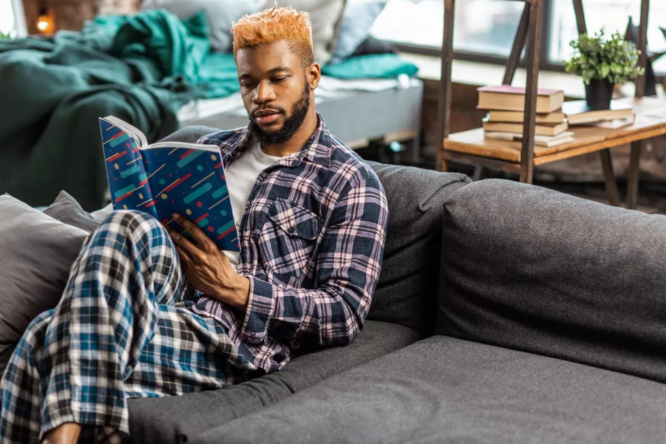Man sitting on the sofa in pyjamas, reading a book