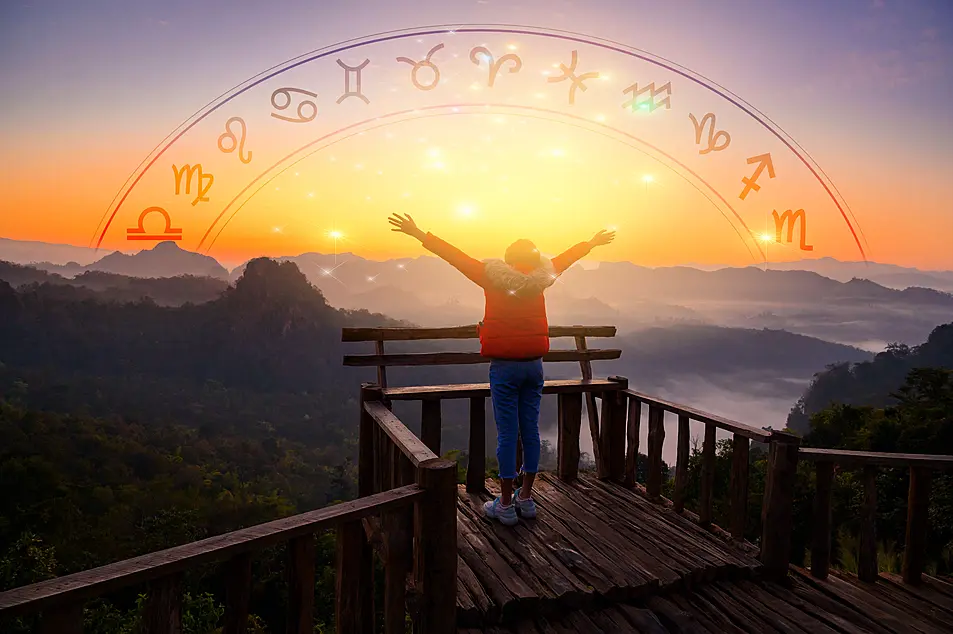 Woman with arms wide open looking at sunrise with zodiac signs in the sky