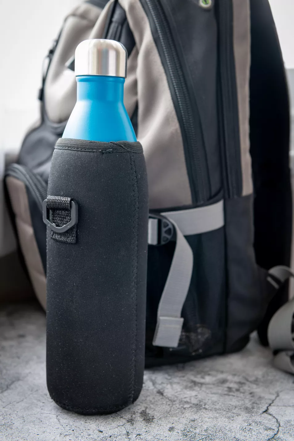insulated reusable water bottle in front of a backpack