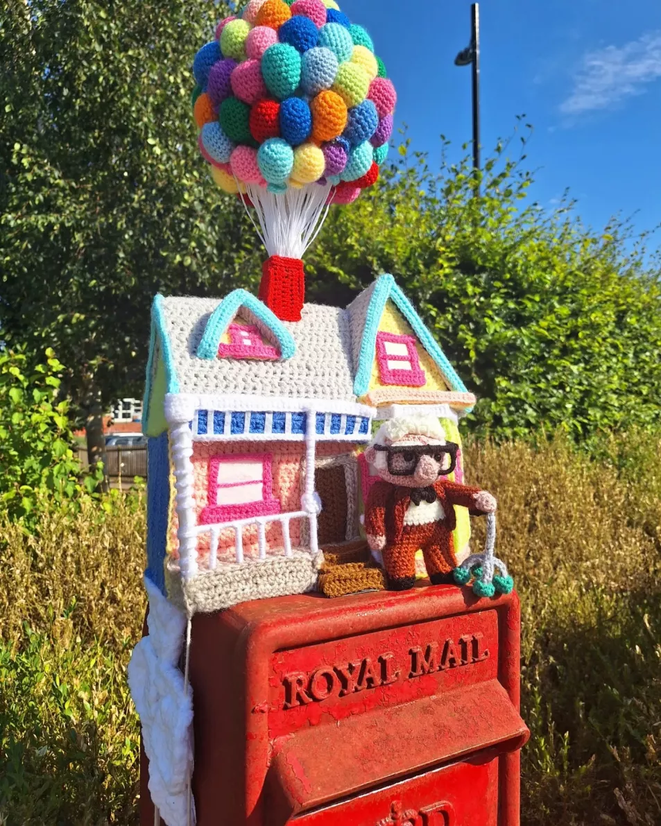 Crocheted house and man on top of a postbox 