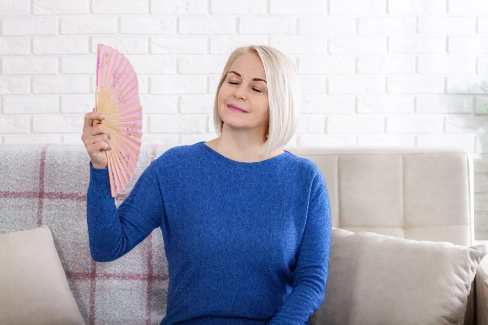 Mature woman experiencing hot flush from menopause. This photo captures the discomfort of hot flashes during menopause, as a woman struggles to cool