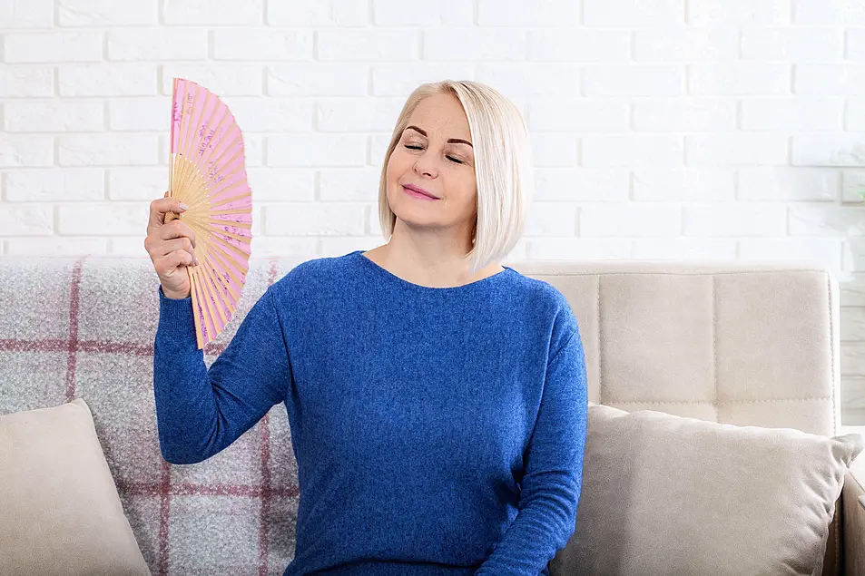 Mature woman experiencing hot flush from menopause. This photo captures the discomfort of hot flashes during menopause, as a woman struggles to cool