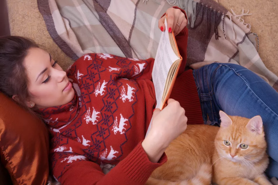 A woman snuggled on the sofa with her cat, reading a book