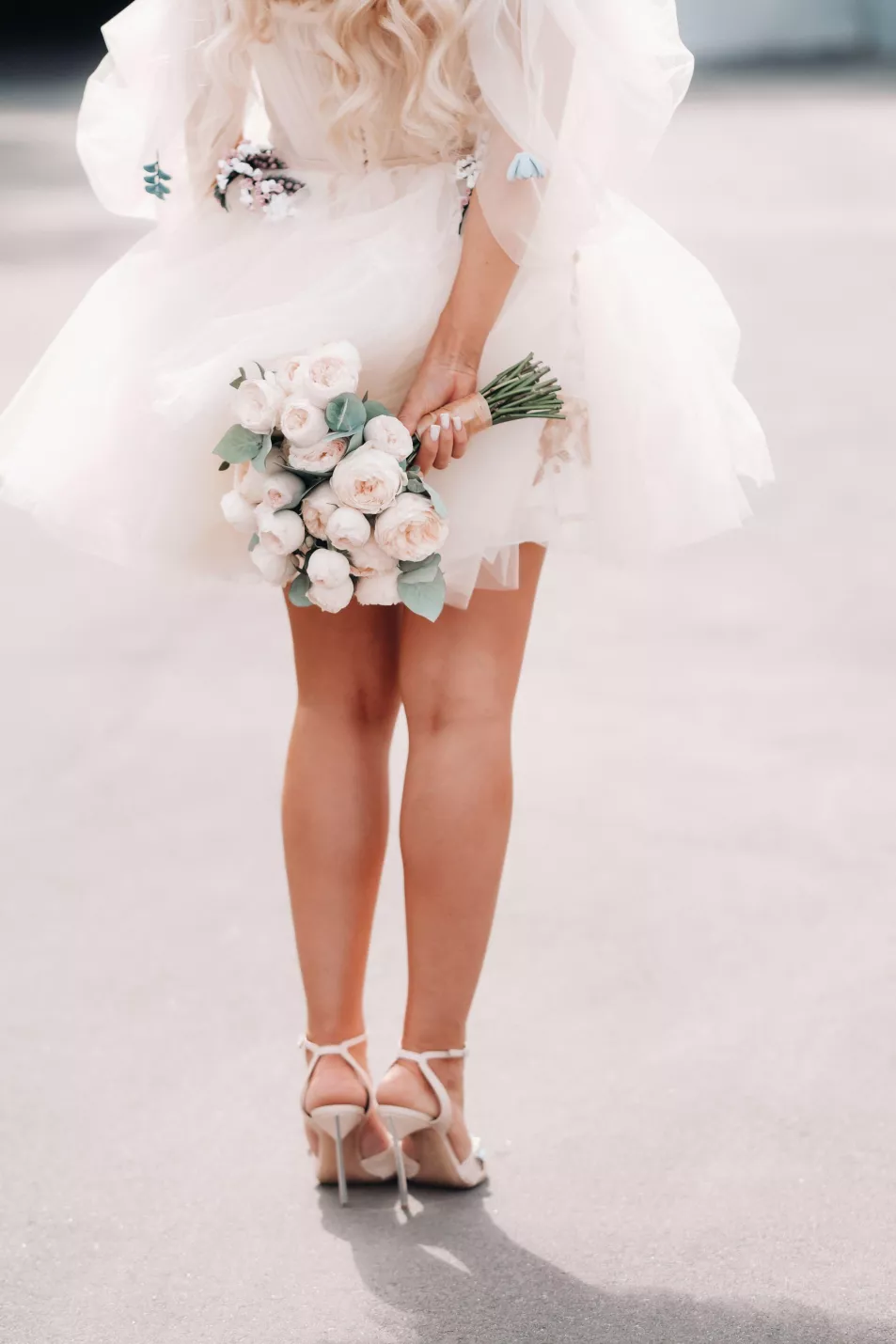 A bride with a short wedding dress holds a bouquet behind her back