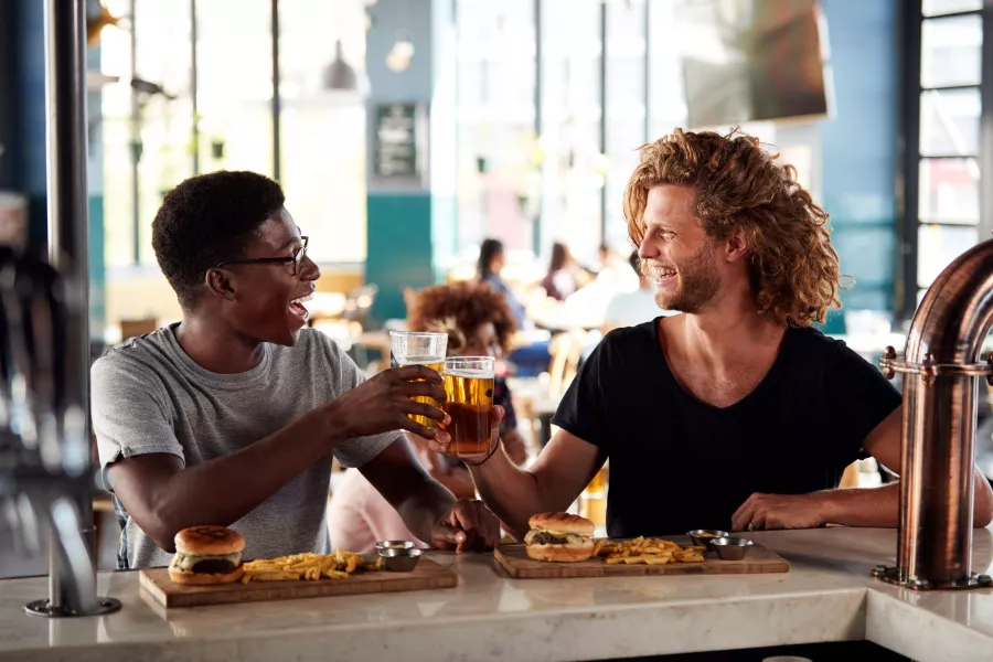Two Male Friends Eating Food And Drinking Beer In Sports Bar