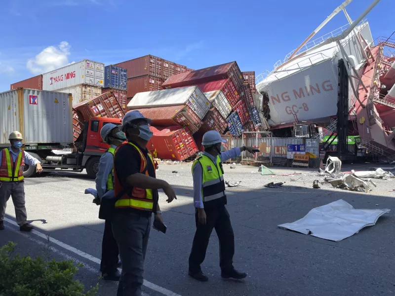 Port workers view the scene after the crane toppled over