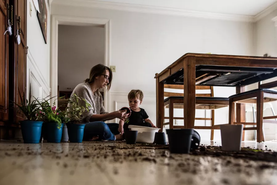 Mother and young son sit on kitchen floor with plants