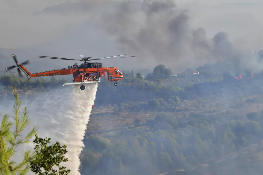 An helicopter drops water during a wildfire in ancient Olympia,