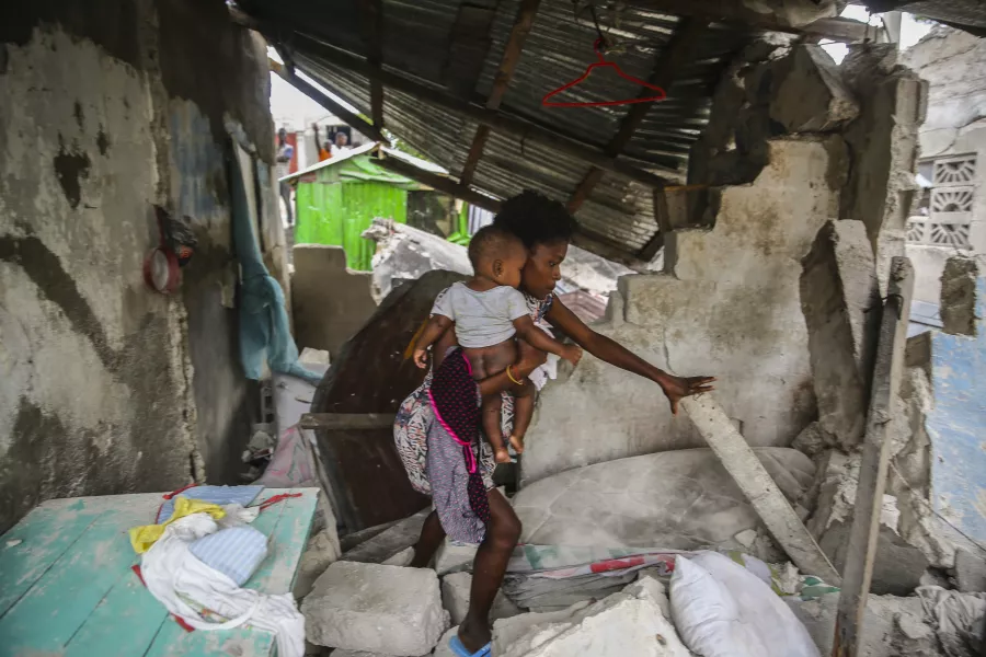 A woman carries her child as she walks in the remains of her home destroyed by Saturday´s 7.2 magnitude earthquake in Les Cayes, Haiti