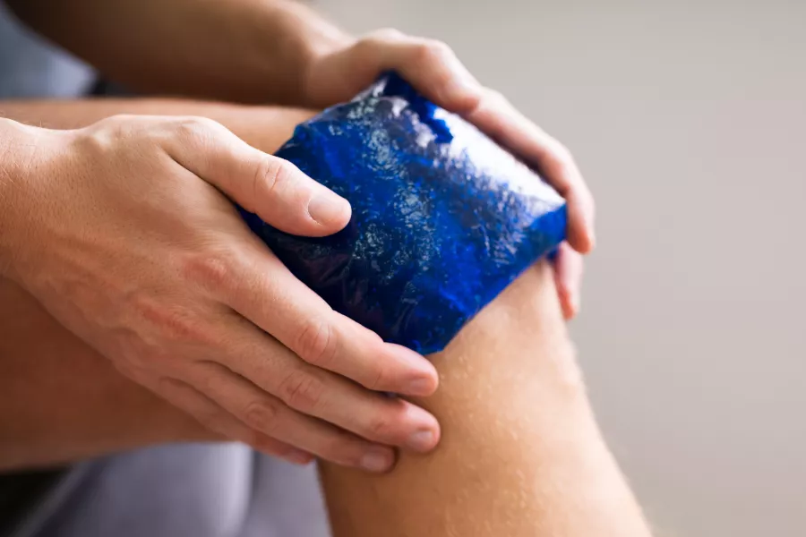 Midsection Of Man Holding Cool Gel Pack On Knee For Pain Relief Over White Background