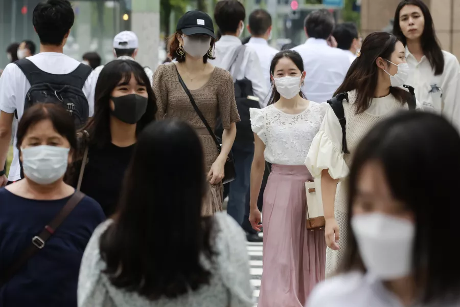 People wearing face masks to help protect against the spread of the coronavirus walk across an intersection 
