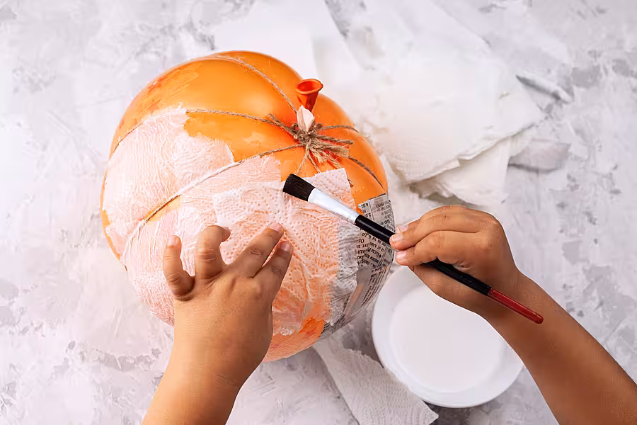 Child's hands make a papier-mache pumpkin from a balloon