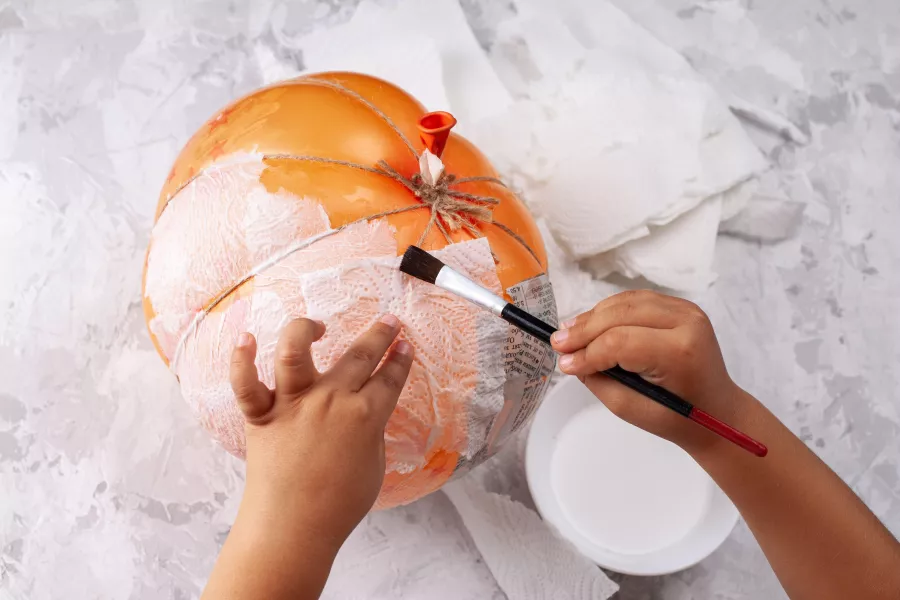 Child's hands make a papier-mache pumpkin from a balloon