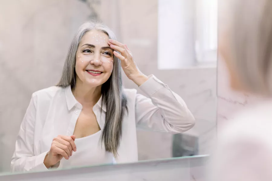 Woman applying skincare in bathroom mirror