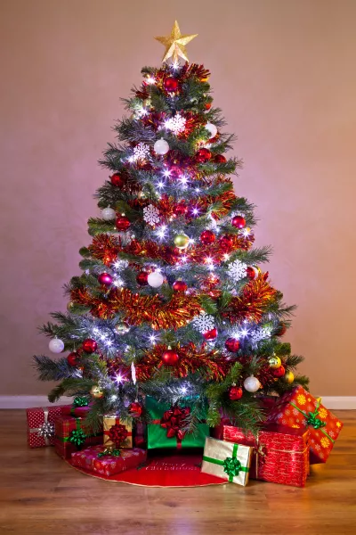 A decorated Christmas tree in a home, lit up with fairy lights and surrounded by gift wrapped presents