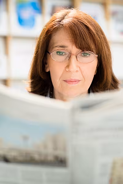 Portrait of middle aged woman with eyeglasses reading newspaper