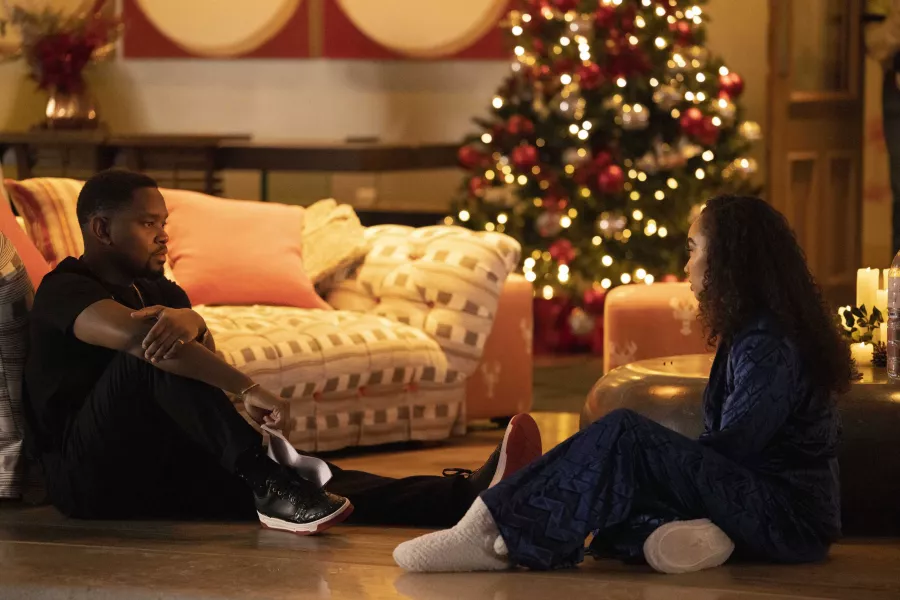 Aml Ameen and Leigh-Anne Pinnock in Boxing Day, both sat opposite each other on the floor of a living room, with a Christmas tree in the background