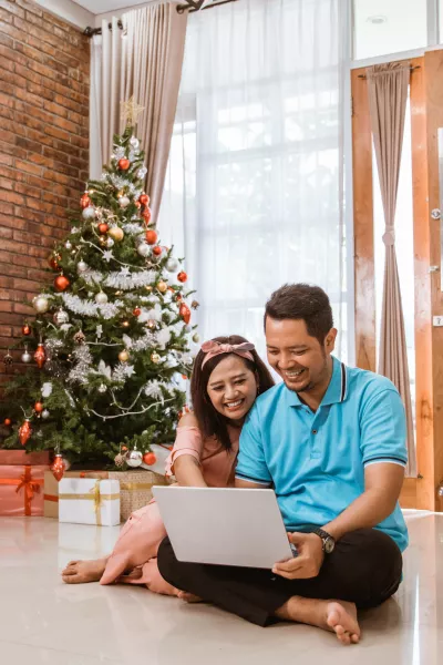 Couple using a laptop next to a Christmas tree