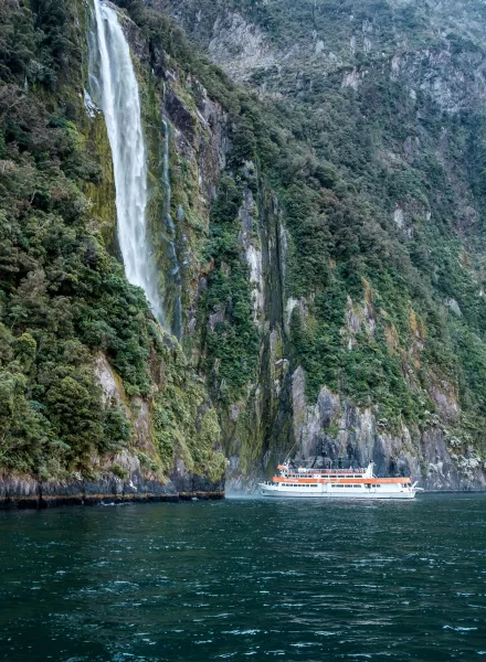 Tourist boat sailing close to waterfall in famous Milford Sound, New Zealand
