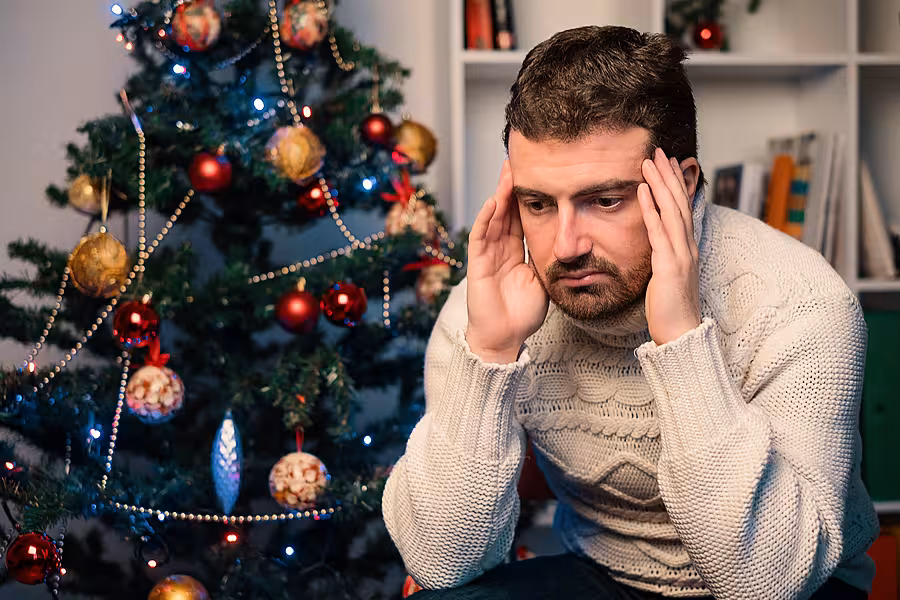 Man sitting by a Christmas tree, with his head in his hands