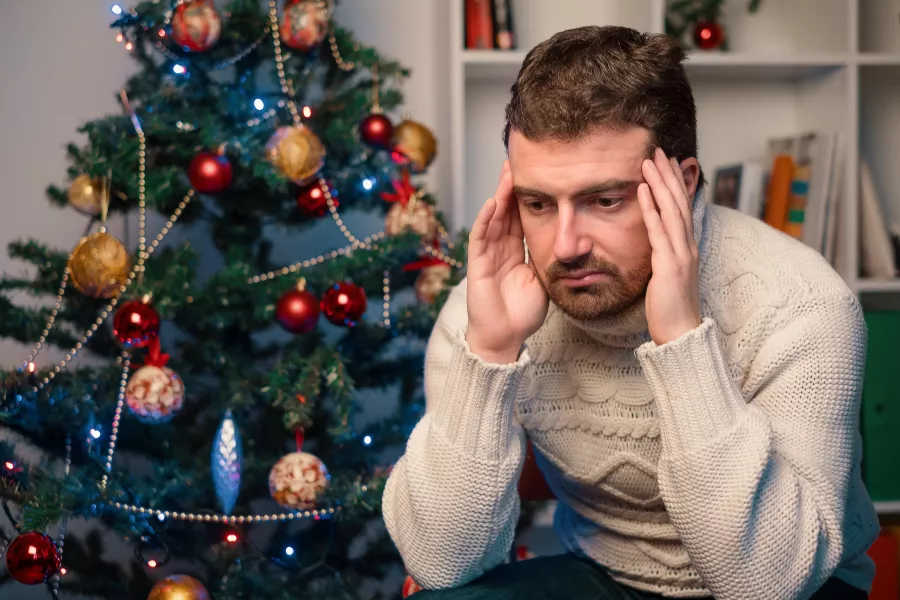Man sitting by a Christmas tree, with his head in his hands