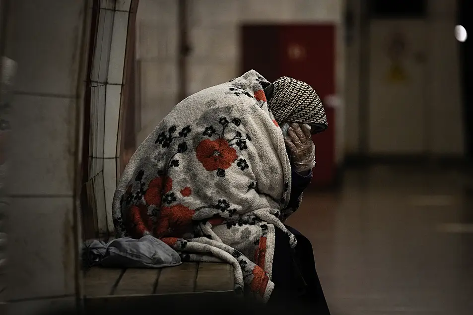 An elderly woman sits on a bench wrapped in a blanket in a subway station turned into a shelter in Kyiv, Ukraine, 