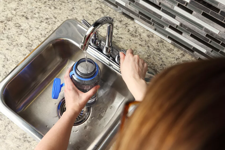 woman filling water bottle from the kitchen tap