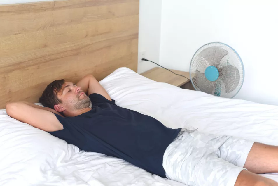 man sleeping with a fan in his bedroom