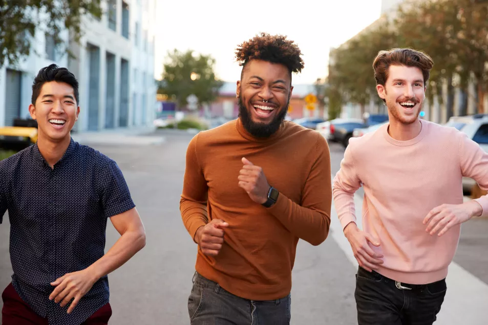 Male friends running down a street laughing together