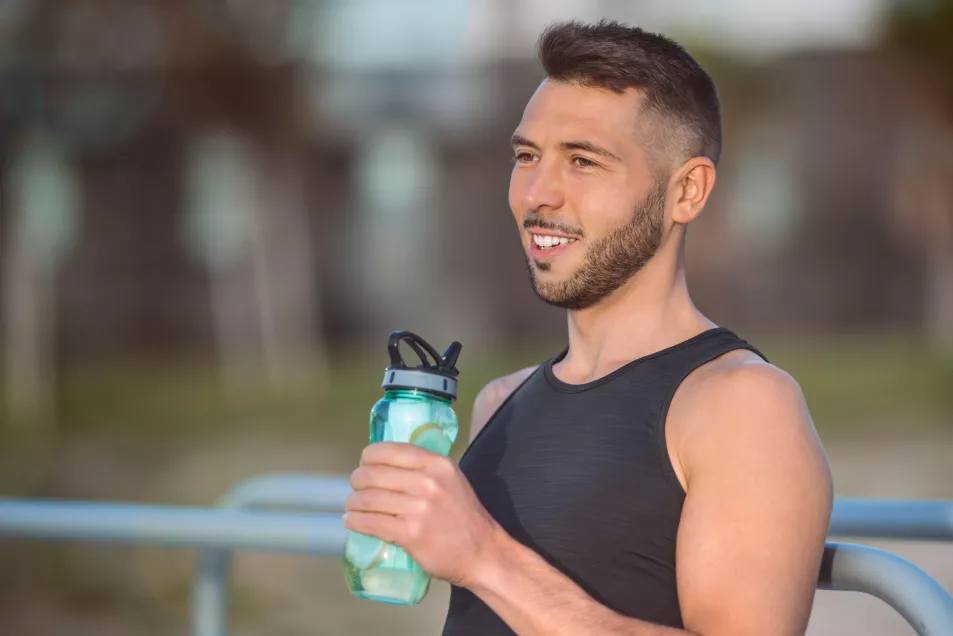 Man drinking water from a reusable bottle while outdoors on a summer's day