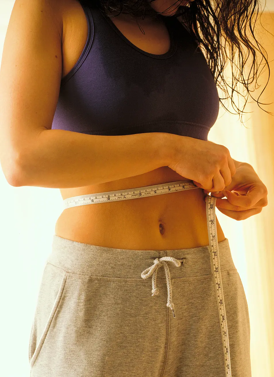 A white woman measuring her waist with a tape measure.