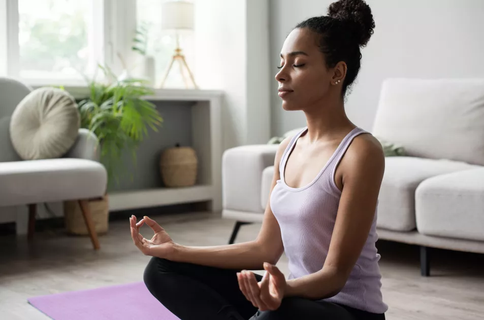 Black woman sitting on the floor at home, doing deep breathing exercises