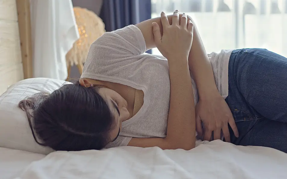 A woman lying on a bed, clutching her abdomen in pain