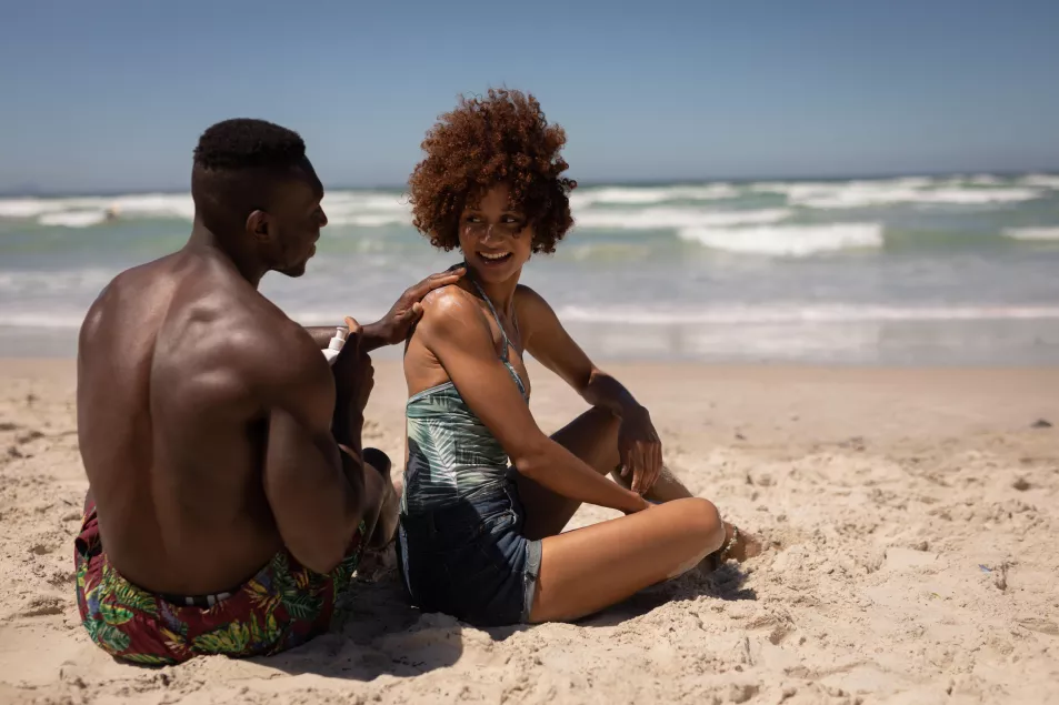 Man applying sunscreen lotion on woman's body at beach