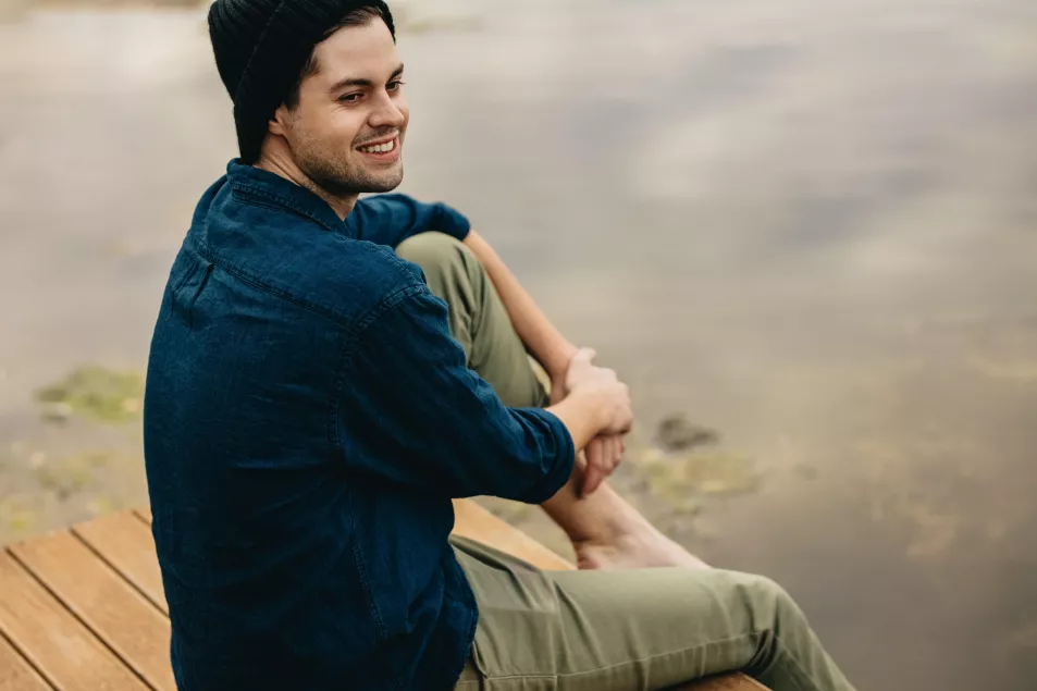 Man sitting on a wooden jetty on a lake, looking relaxed and happy
