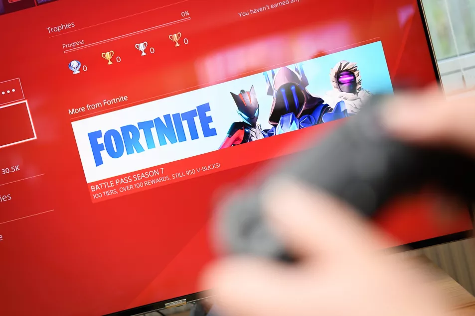 A person holding a controller in front of a screen with a Fortnite image on it 