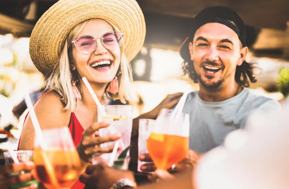 Trendy couple having fun drinking fancy cocktails at beach party - Summer joy and genuine life style concept with young people at festival happy hour