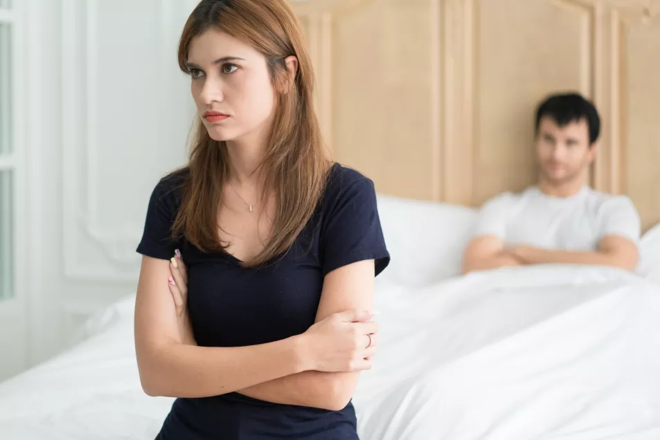 Woman sat at the end of her bed with her arms crossed 