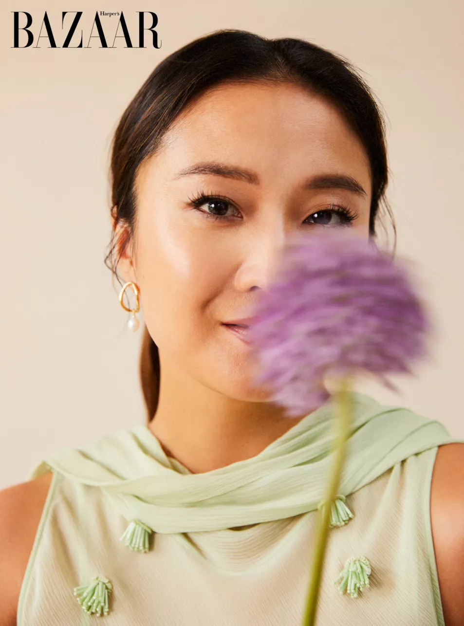 Ashley Park in a green top with a purple flower in front of her face