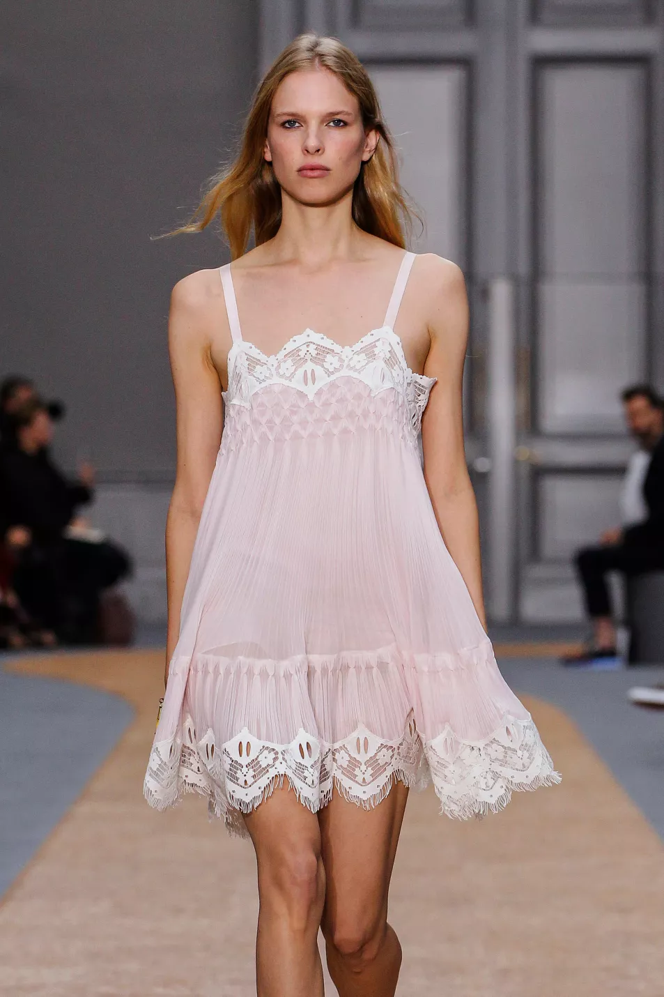 Model walks down runway in pink and white sheer dress with lace trim