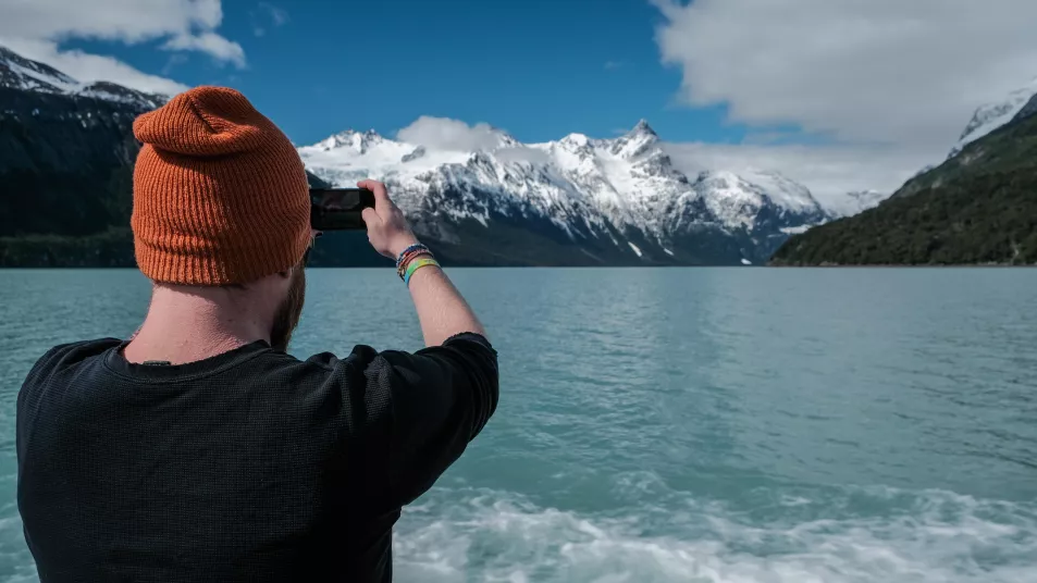 A man taking a photo in Patagonia of water with snow-capped mountains beyond