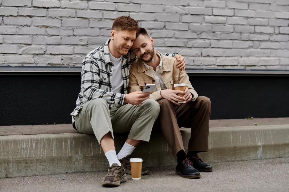 Gay male couple sitting on a wall outside, looking at an iphone screen together