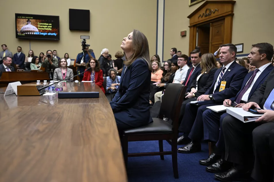 A woman sits at a long table in front of a row of men