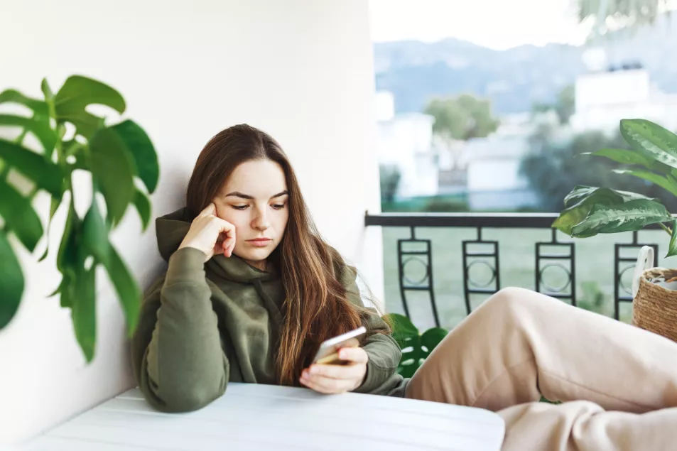 Unhappy young woman sitting on a balcony looking at her phone